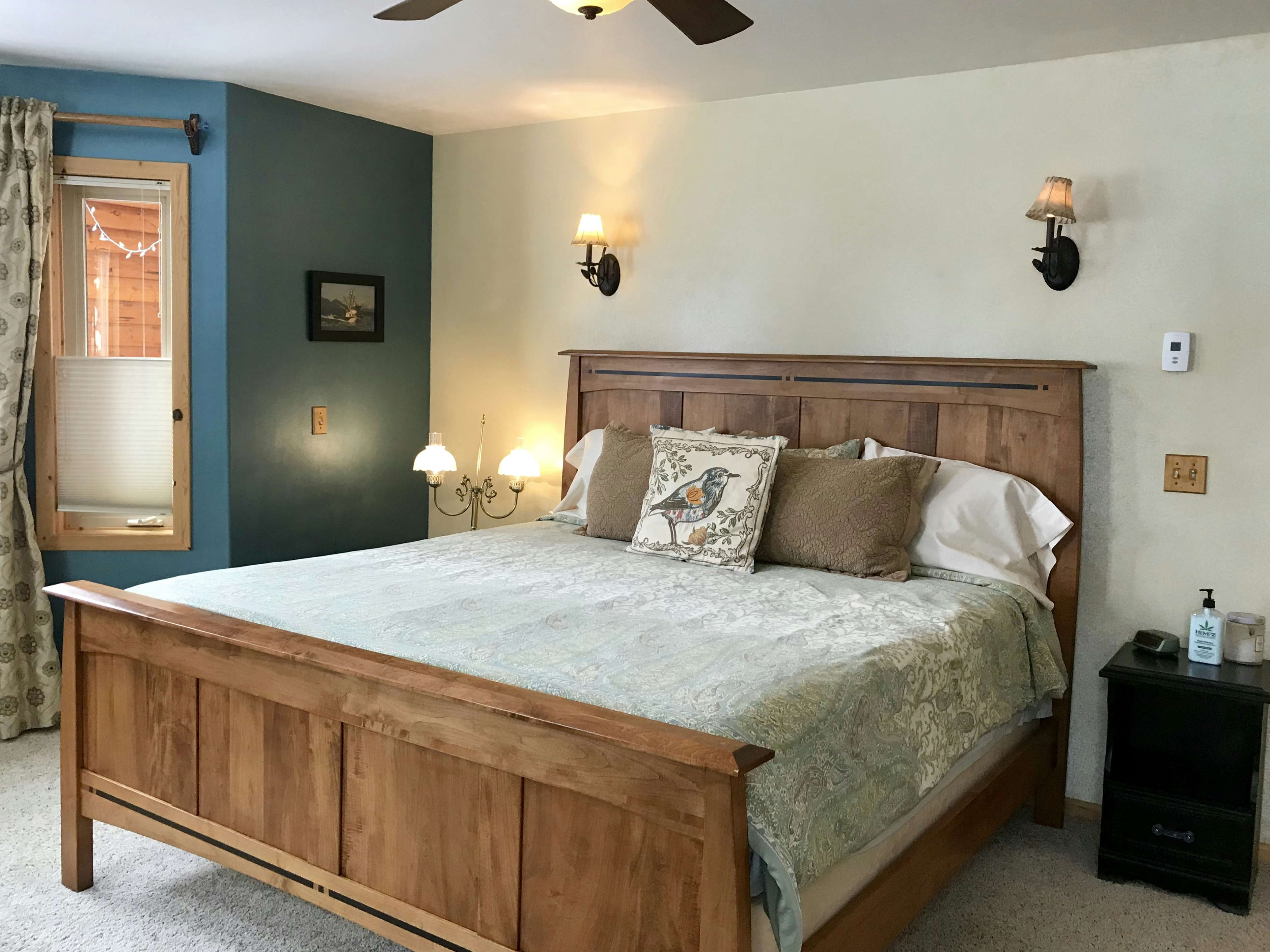 Cozy bed with wooden headboard and footboard, decorative throw pillows, nightstand, and ceiling fan
