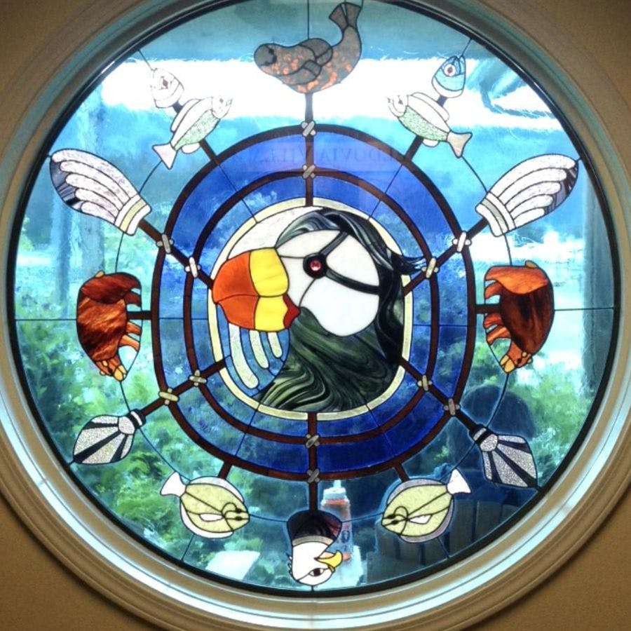 A gorgeous circular stained glass window with a puffin bird in the center and inlaid images of fish all around