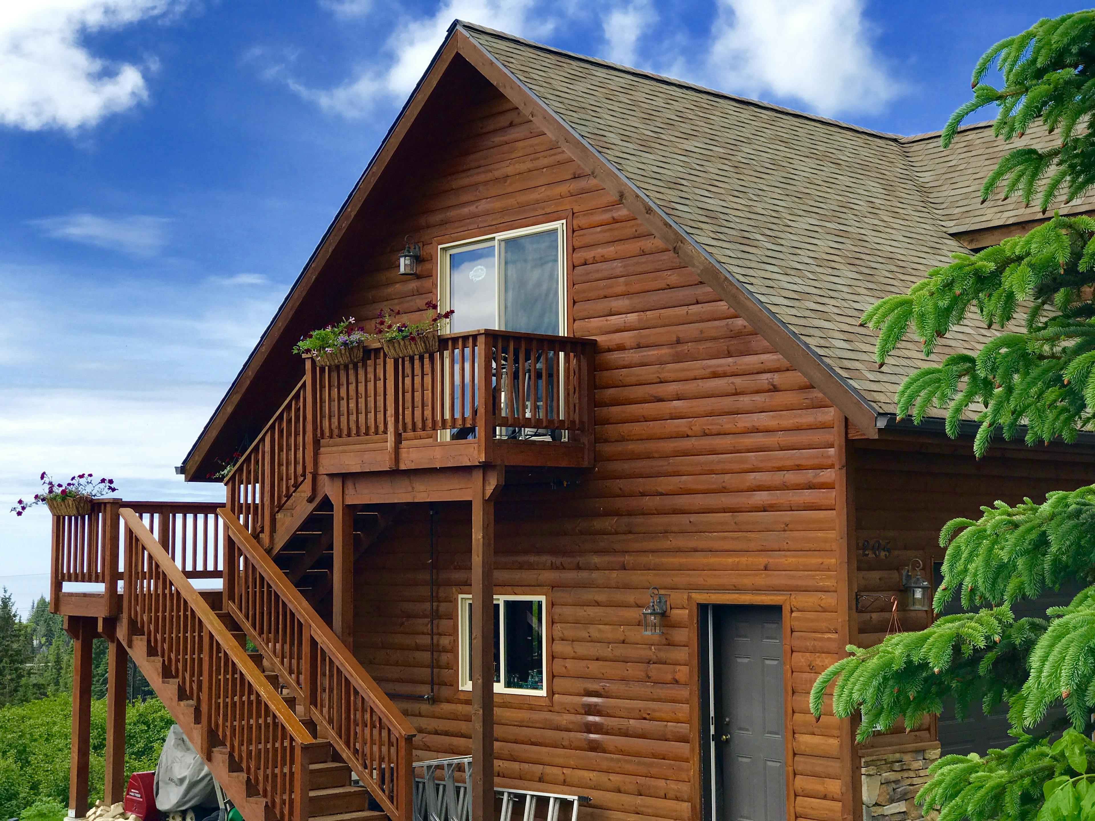 Exterior of two story log home with exterior stairs, trees, and bright blue sky
