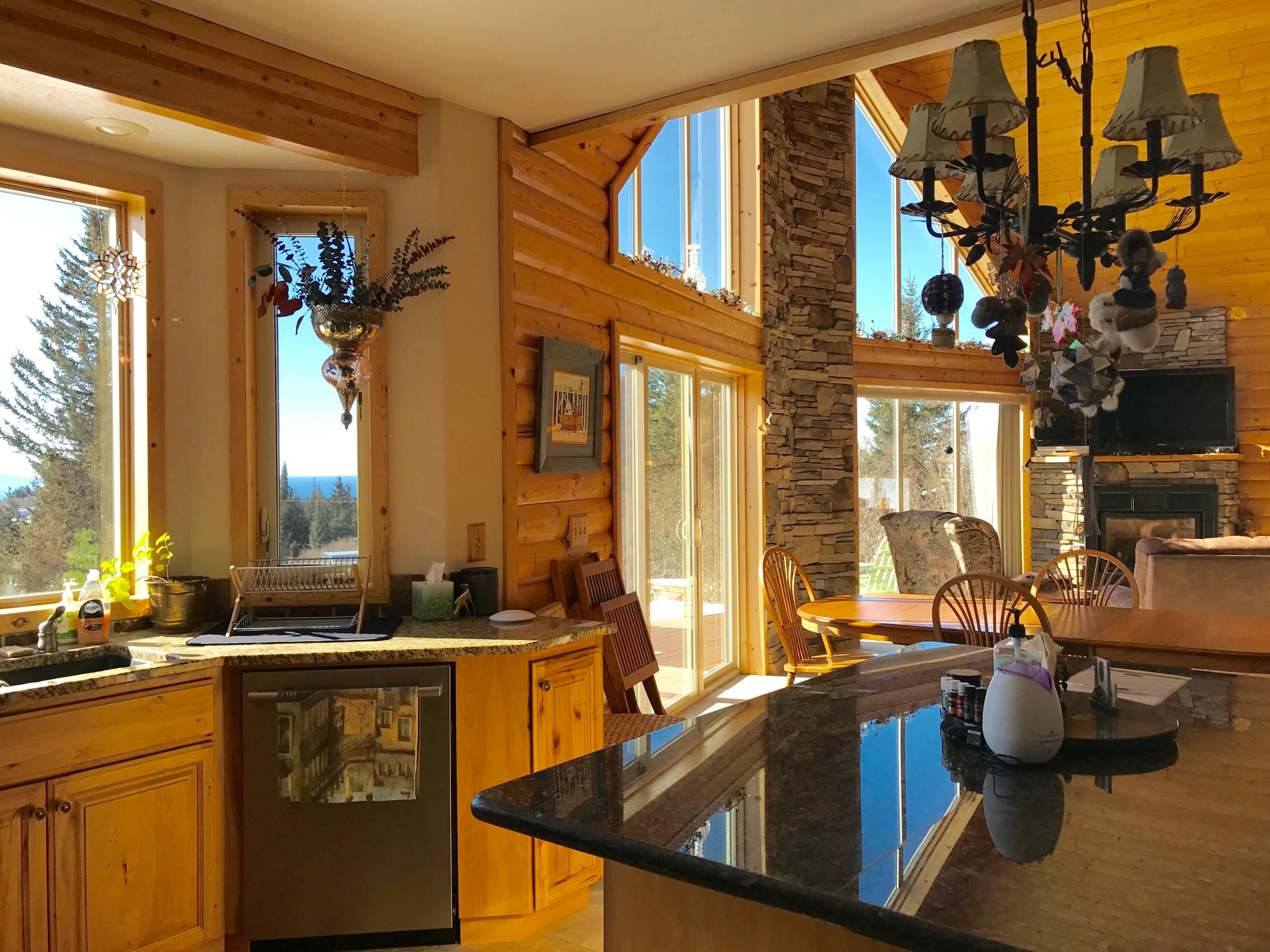 View of the great room from the kitchen, counter with sink to left, kitchen island to right with two-story windows, fireplace, and sitting area in background