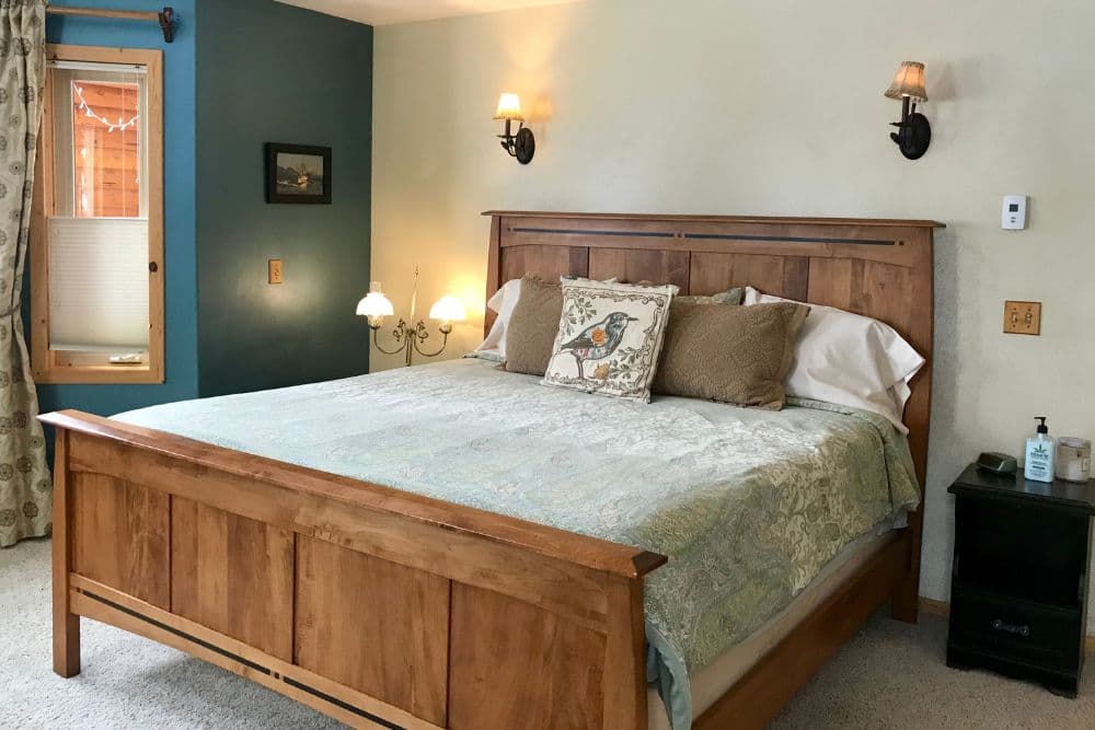 Bedroom with cream and blue walls, king bed with wood headboard and footboard, window with curtains