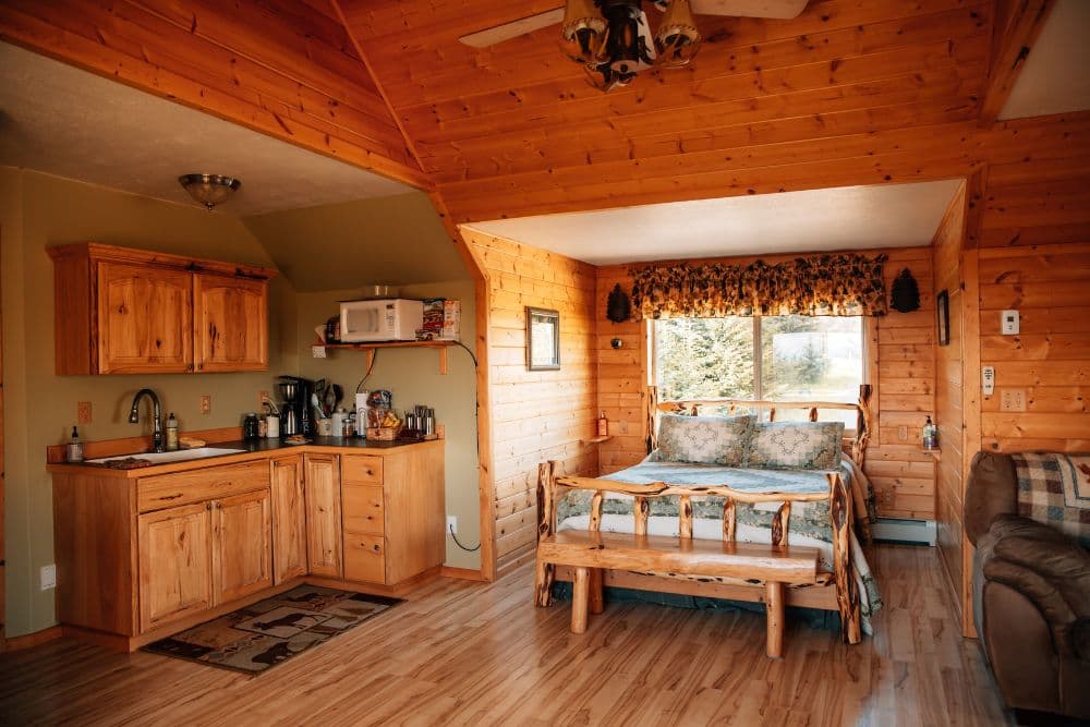 Spacious suite of a log home with a bed in a nook by a large window, kitchenette and couch.