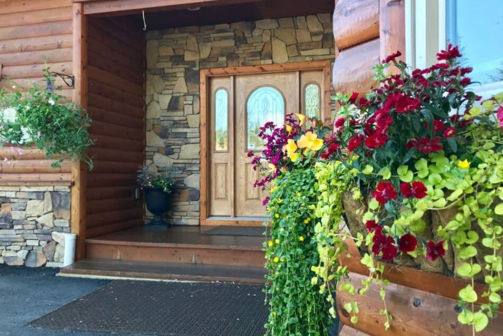 Front door of an elegant log cabin home with gorgeous potted flowers