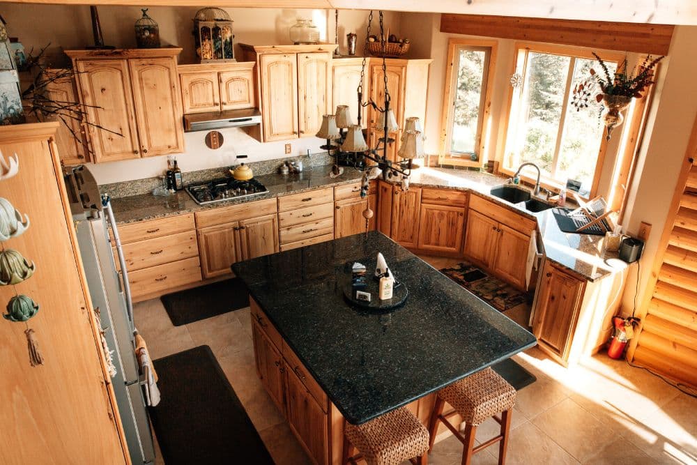 Large kitchen with light oak cabinets, center island with black countertop and two stools and large bay window