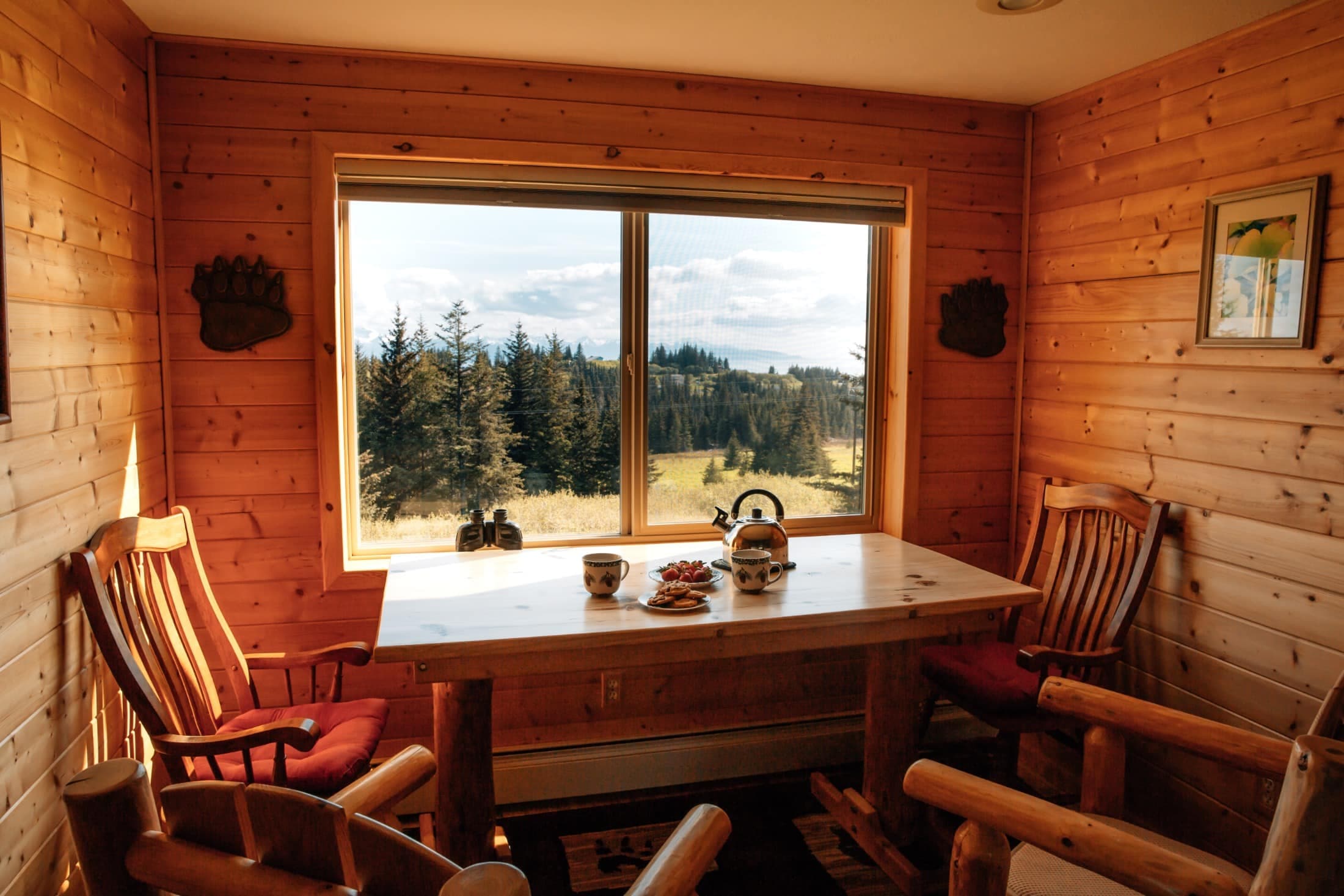 Pine table in nook area with 2 chairs with wood pine board walls looking out over sliding doors into outdoors