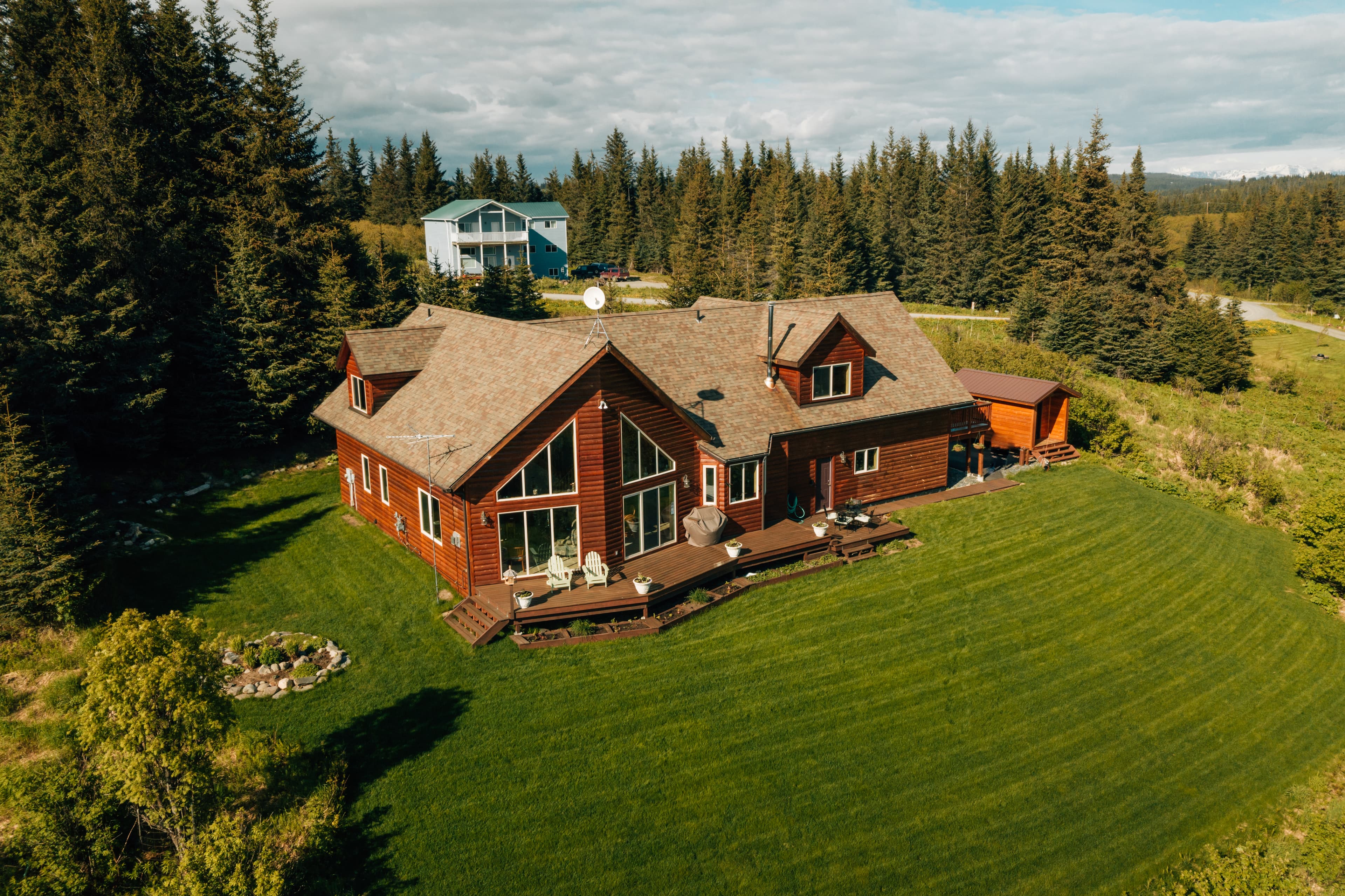 Front of Cozy Cove Inn with high windows, deck, bird feeder, gardens, and potted flowers .