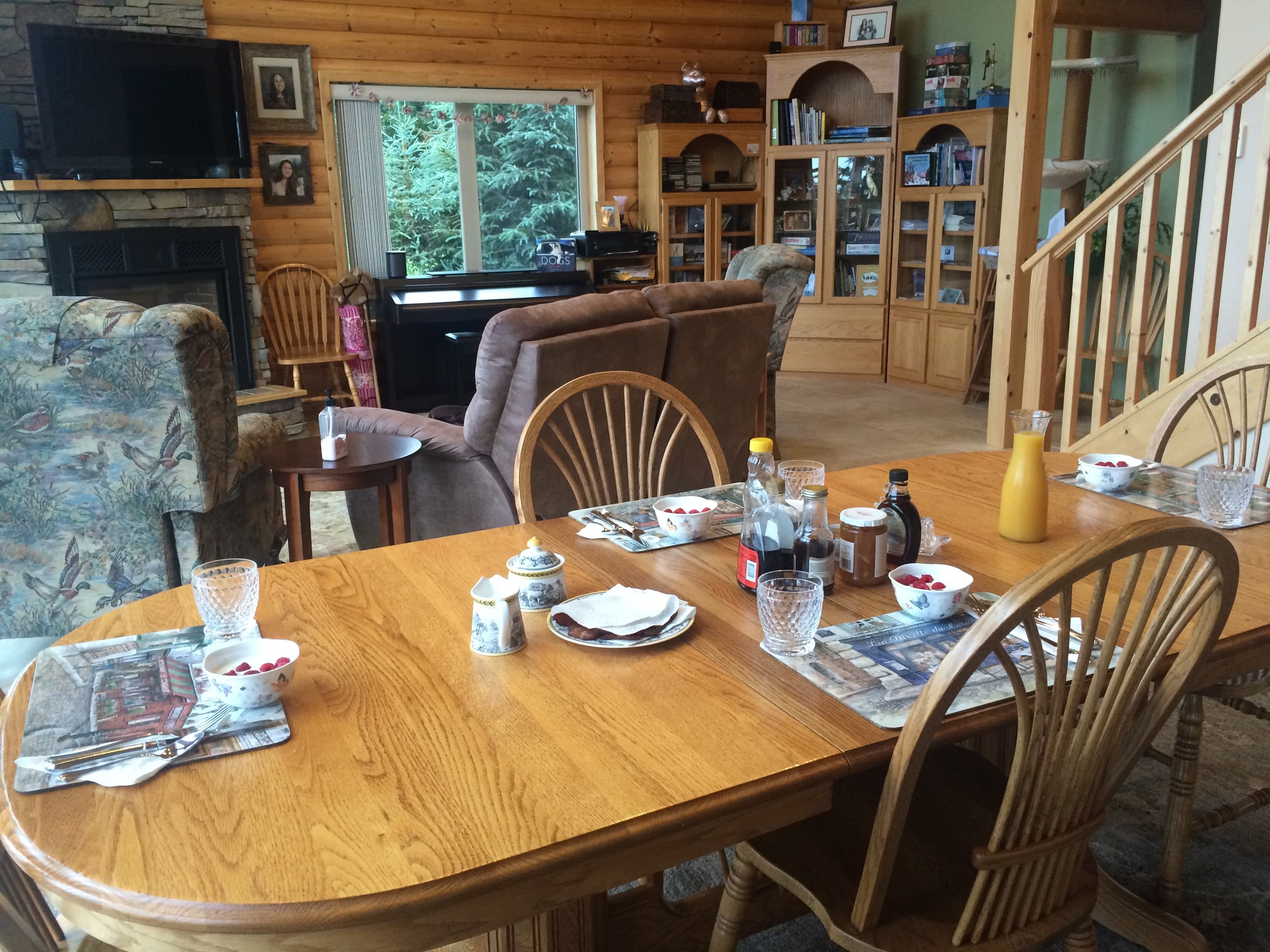 table set for a yummy breakfast with rest of the great room in background including bookshelves, large tv, fireplace, and living room furnishings.