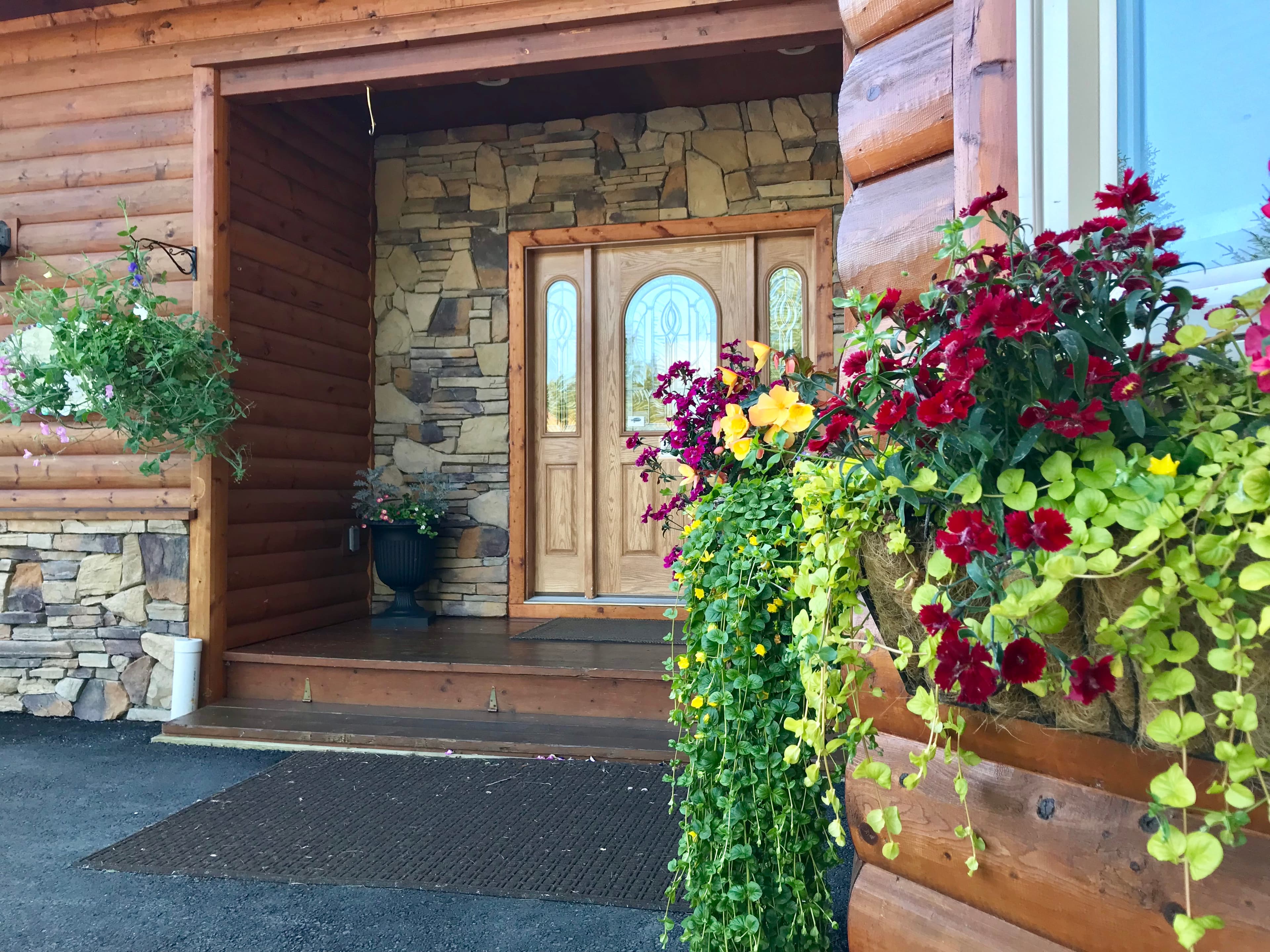 Entrance to The Main House featuring a beautiful wood door surrounded by stone, potted flowers and trailing vines