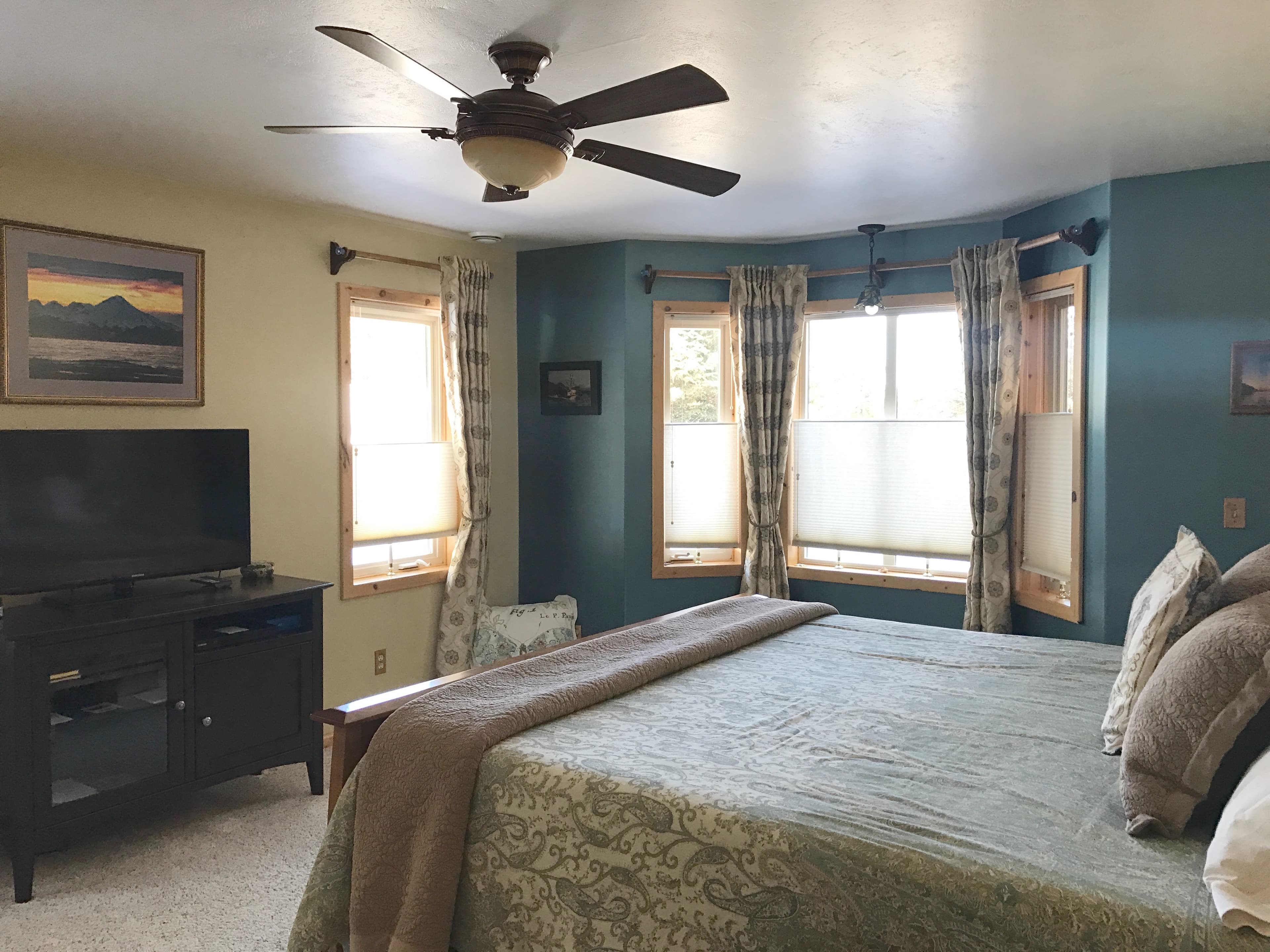 Bedroom with inviting bed, ceiling fan, bay window, console with flat-screen TV